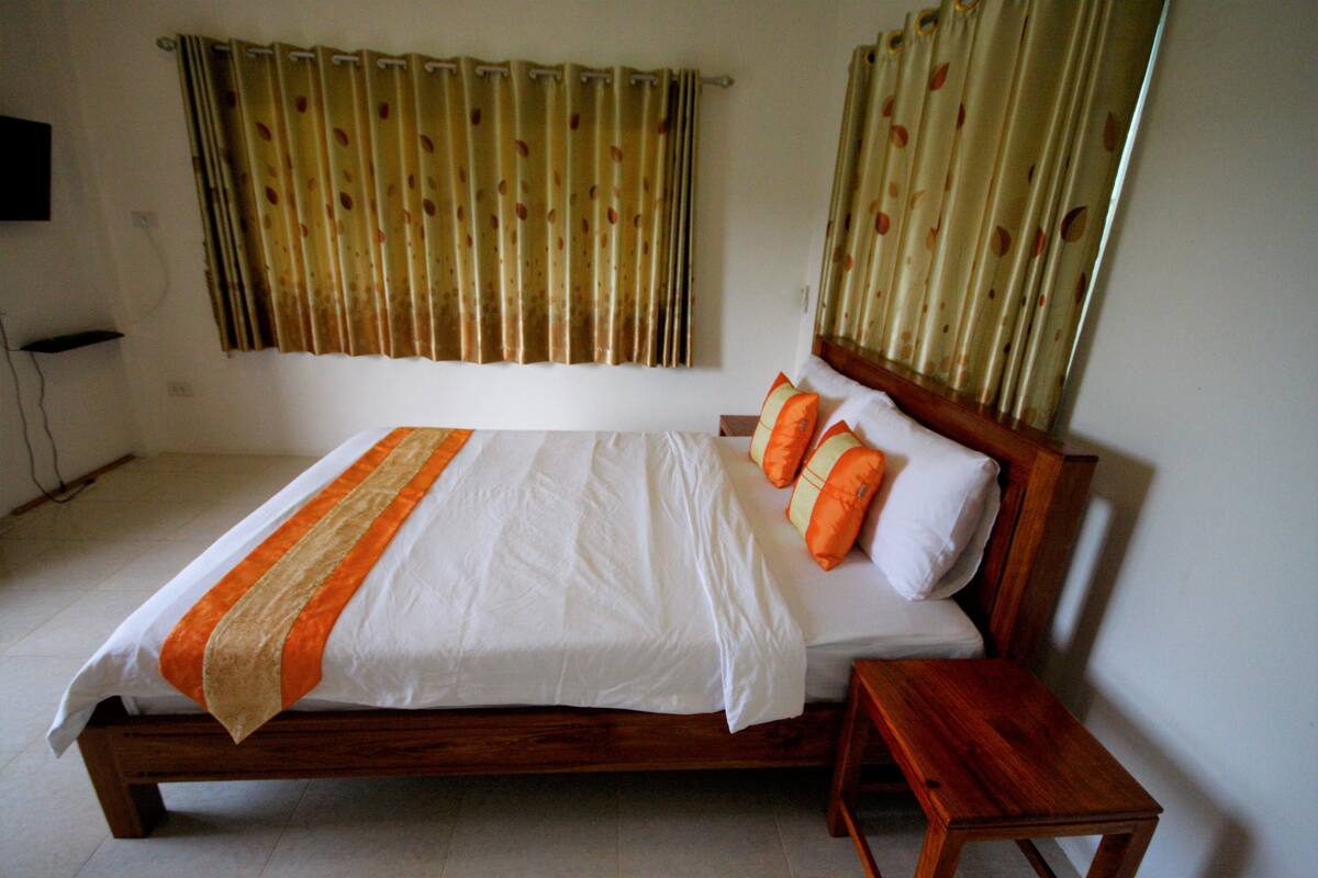 A neatly made bed with a wooden frame, white bedding, and orange accents.