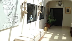 A sunlit hallway with a white bench, a potted plant, and a door with a framed picture above it. - Domus Felix (Sorrento)