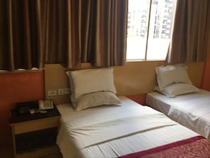 Habitación de hotel con dos camas individuales, una mesita de noche con teléfono y una ventana con cortinas.
