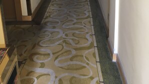 A hallway with patterned carpet, a visible exit sign, and a door on the left. - Victory hotel (Guangzhou)
