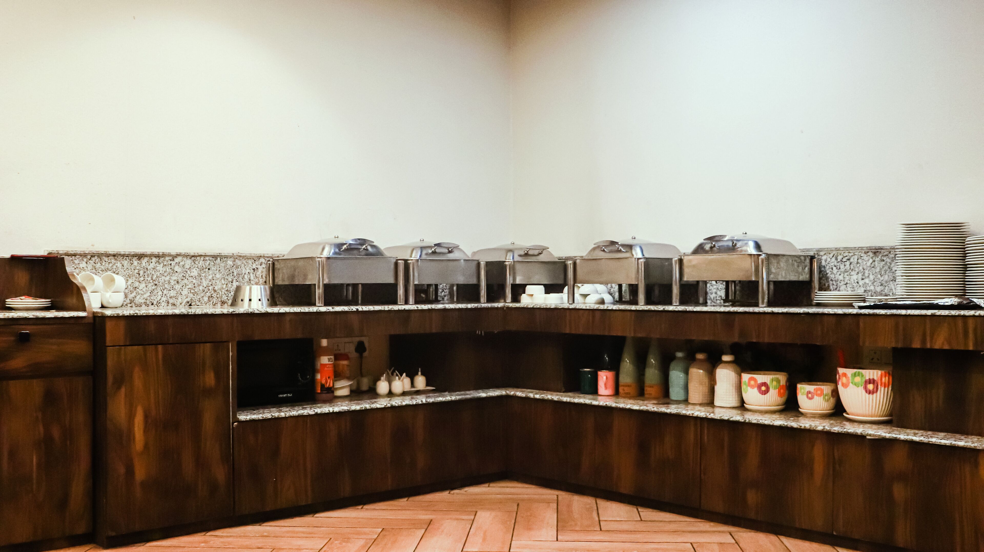 A buffet setup with multiple food dispensers, a variety of condiment bottles, and stacked plates on a granite countertop.