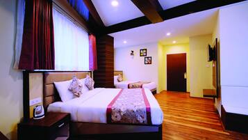A hotel room with a large bed, a bedside table with a kettle, a wooden floor, and a door leading to another room.