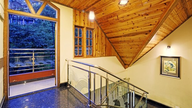 Un escalier avec des rampes en verre menant à un balcon doté de grandes fenêtres donnant sur une zone boisée.