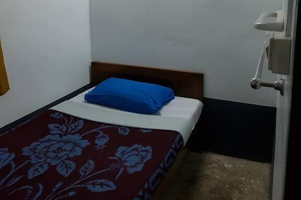 Quarto pequeno, com uma cama de casal, cabeceira de madeira, travesseiro azul e colcha estampada.
