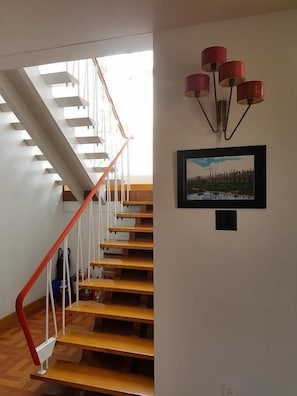 A staircase with wooden steps and a red handrail, leading to a landing with a framed picture and a red pendant light fixture. - Parami Motel (Kalaw)
