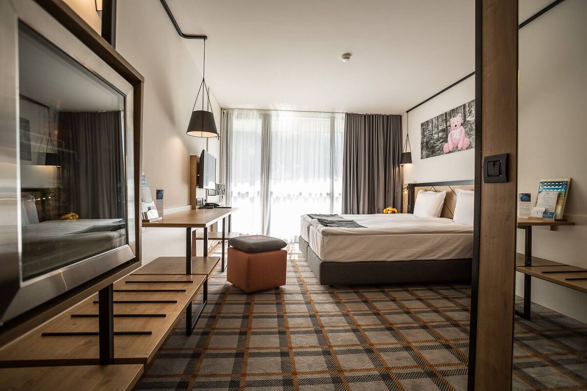 A hotel room with a bed, a desk, a television, and a window with curtains.