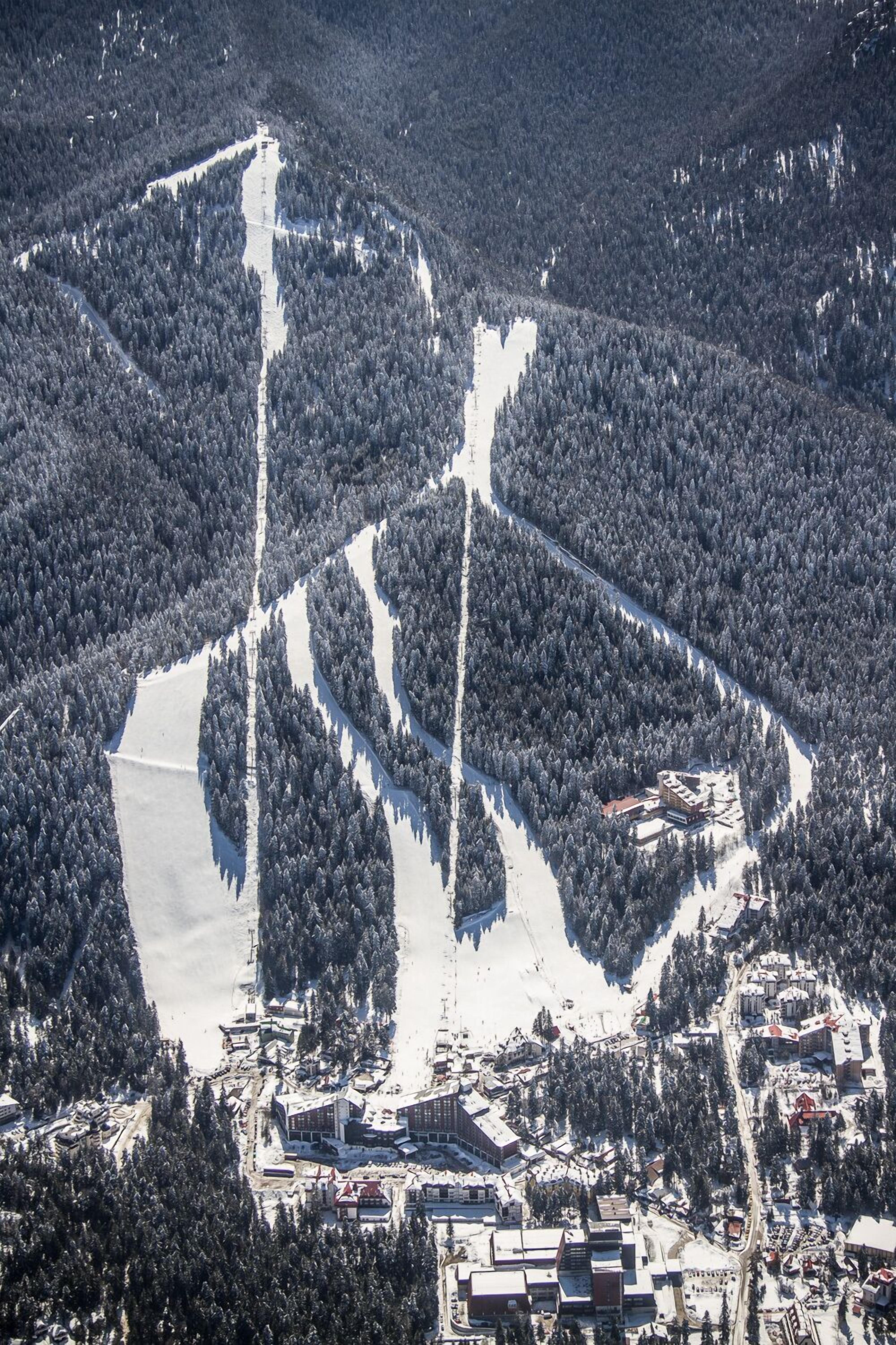 An aerial view of a ski resort with multiple buildings, ski trails, and a large body of snow-covered water.