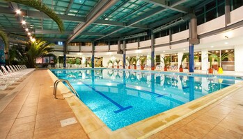Piscina interna com água azul cristalina, rodeada por espreguiçadeiras e plantas em vasos.