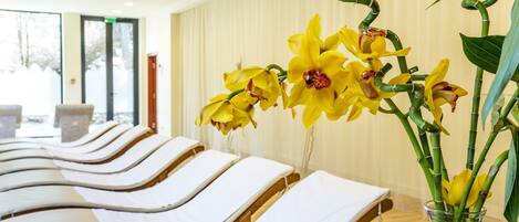 A room with rows of sun lounger beds and a vase of yellow orchids.