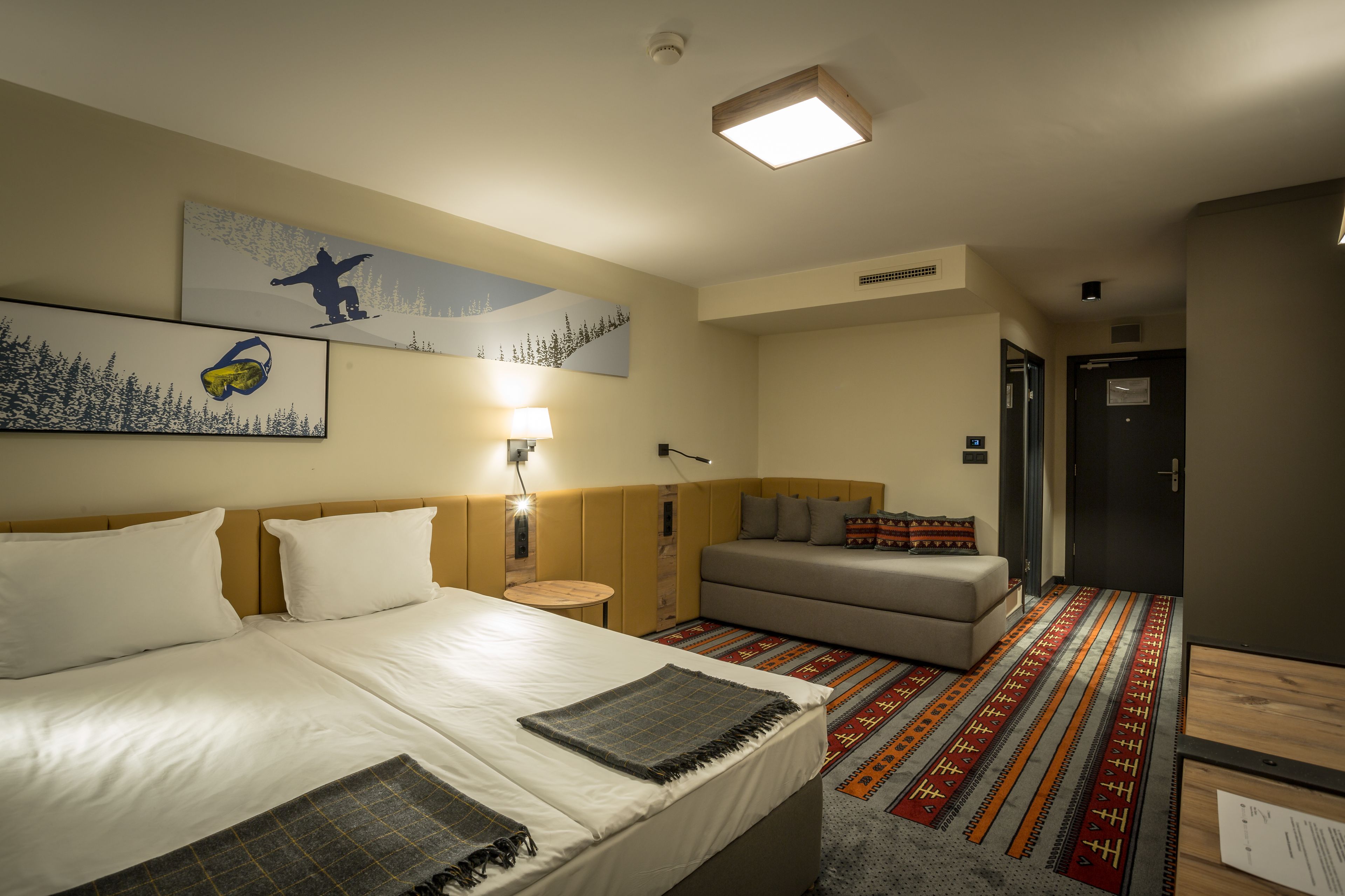 A hotel room with a bed, a sofa, a small table, and a wall-mounted lamp.
