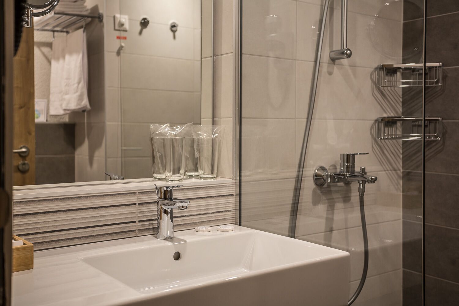 A modern bathroom with a white sink, glass shower enclosure, and a mirror above the sink.