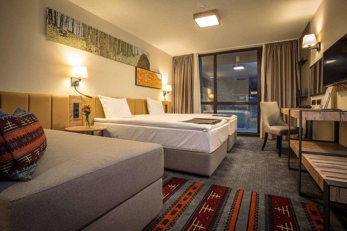 A hotel room with two beds, a desk, a chair, a TV, and artwork on the walls.