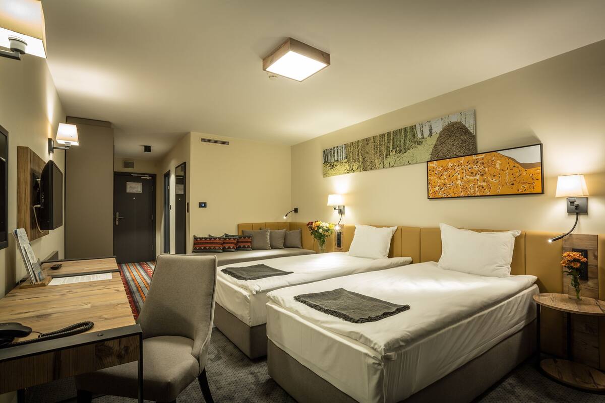 A hotel room with two beds, a desk, a chair, a lamp, and artwork on the wall.