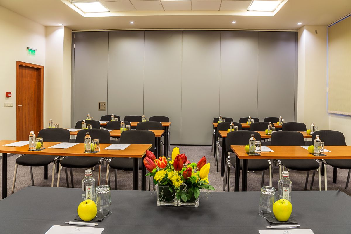 Una sala conferenze con tavoli, sedie e centrotavola floreali.