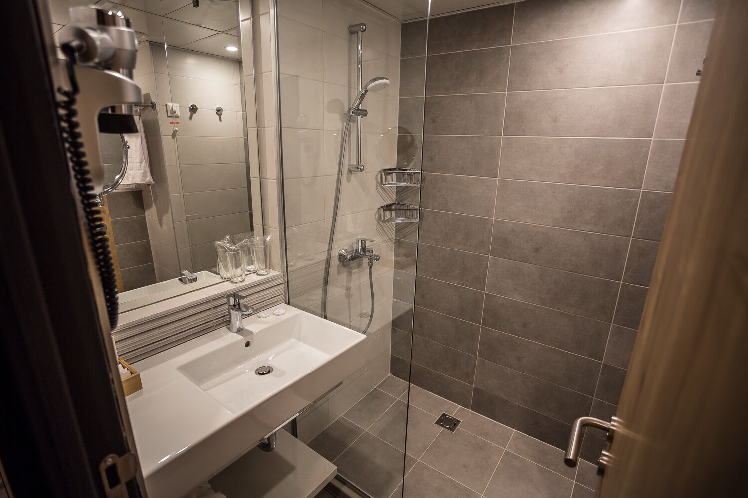 Un baño moderno con ducha de vidrio, un lavabo blanco y un espejo.