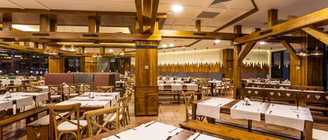 Un restaurante con vigas de madera, mesas dispuestas con manteles blancos y un ambiente cálido.