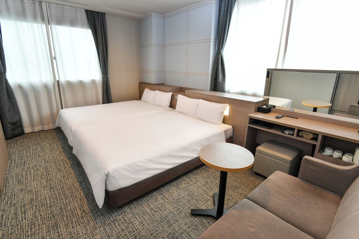 Habitación de hotel con una cama grande, un escritorio con silla, una mesita redonda y un televisor.