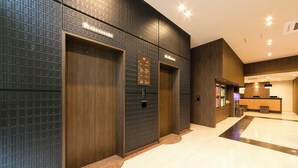 Un hall d’entrée moderne avec un comptoir d’accueil, des ascenseurs et un mur décoré de motifs.