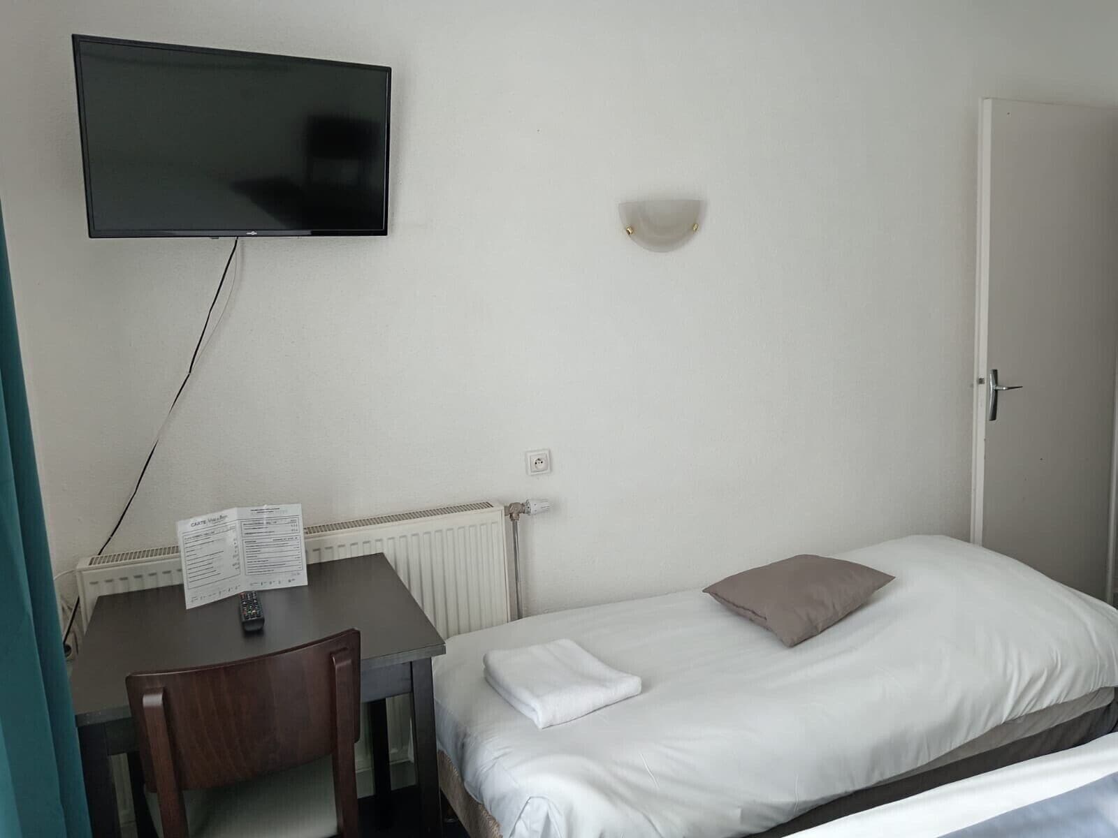 Habitación de hotel con cama, escritorio, silla, televisor montado en la pared y puerta.