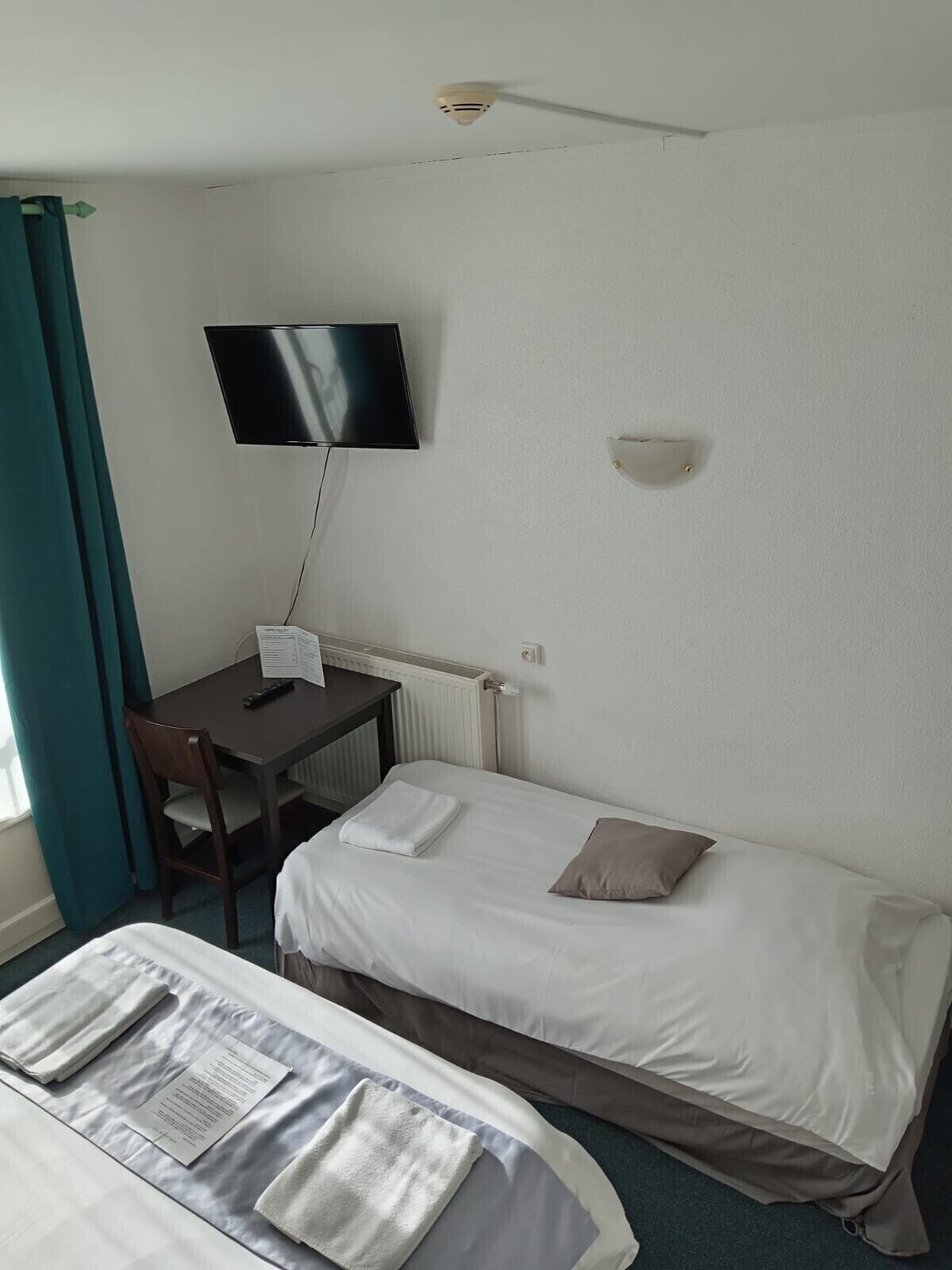 Une chambre d’hôtel avec deux lits, un bureau doté d’un téléviseur à écran plat, une chaise et une fenêtre avec des rideaux.
