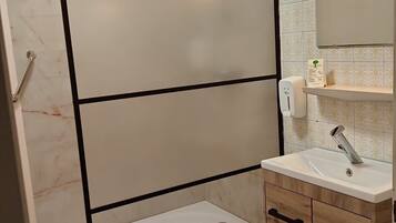 A modern bathroom with a glass shower enclosure, a sink with a mirror, and a wooden cabinet.