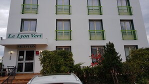 A multi-story building with balconies, a reception area, and a sign reading "Le Lyon Vert".