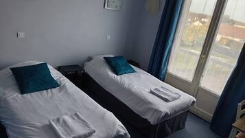 A hotel room with two single beds, a small table, a chair, and a window with curtains.