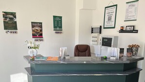 A hotel reception desk with a brown chair, a glass display case, and various informational posters on the wall.