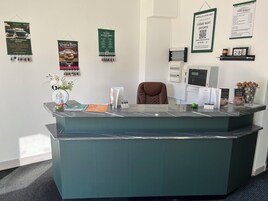 Uma receção de hotel com uma cadeira marrom, uma vitrine de vidro e vários cartazes informativos na parede.