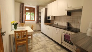 A compact kitchen with a dining table, chairs, a microwave, an oven, and a window with curtains. - Zur Auszeit (Traunreut)