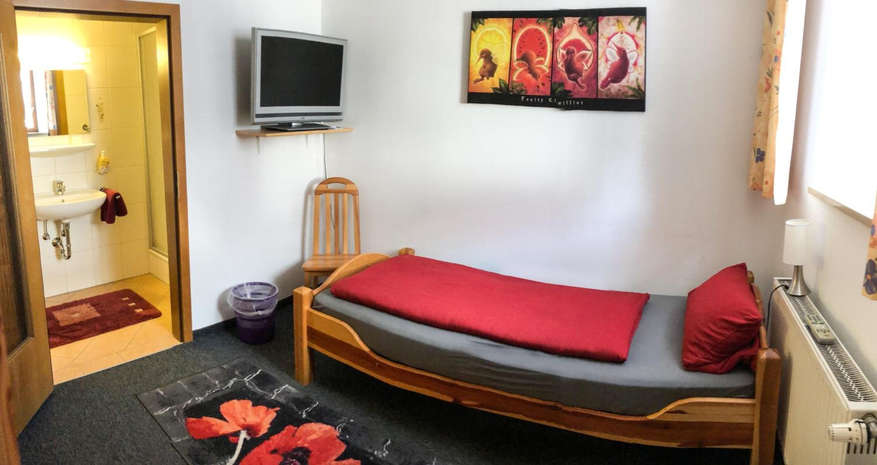 A small bedroom with a single bed, a television, a painting, and a radiator.