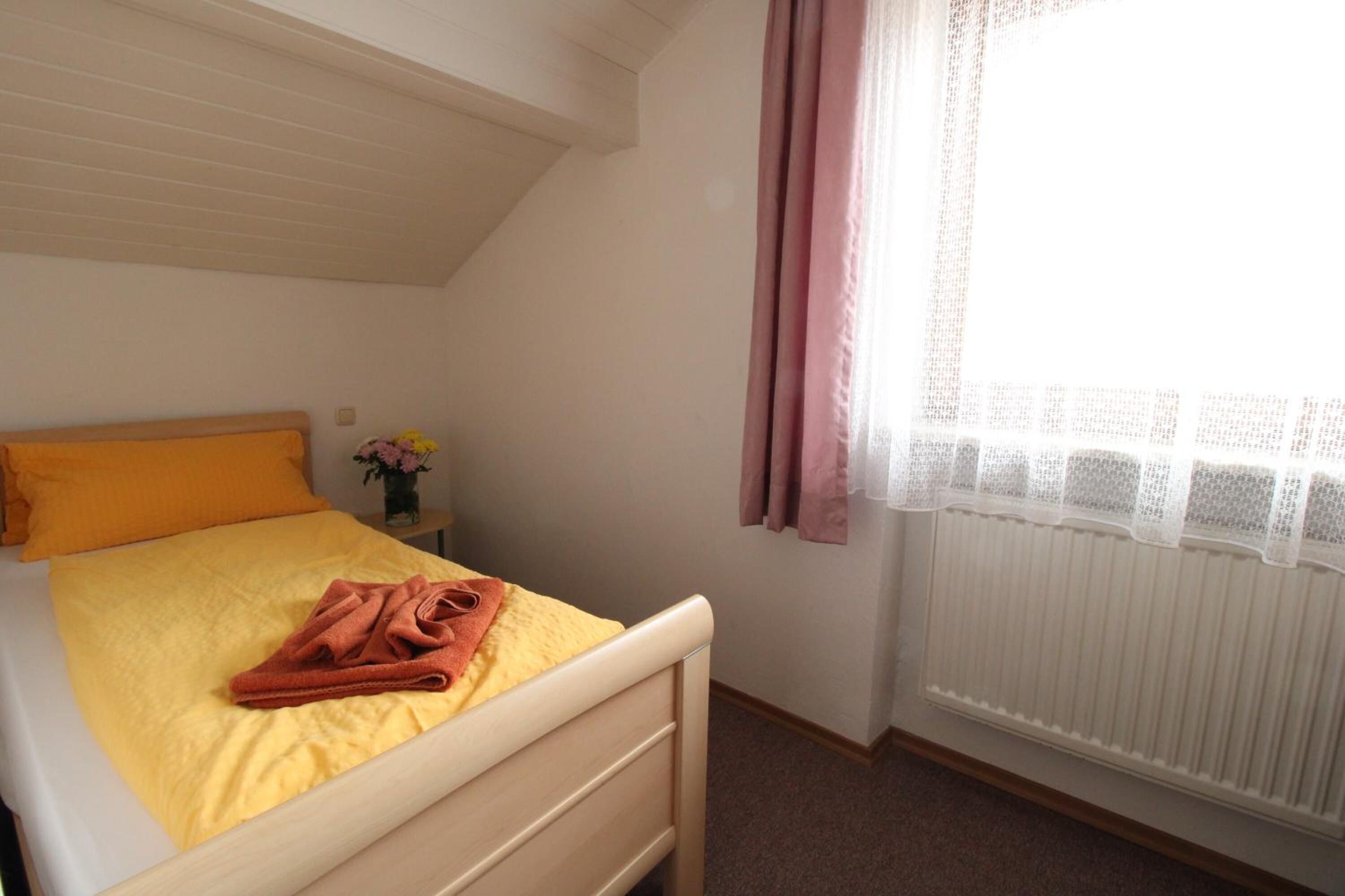 Een slaapkamer met een bed, een nachtkastje met een bloevas en een raam met gordijnen.