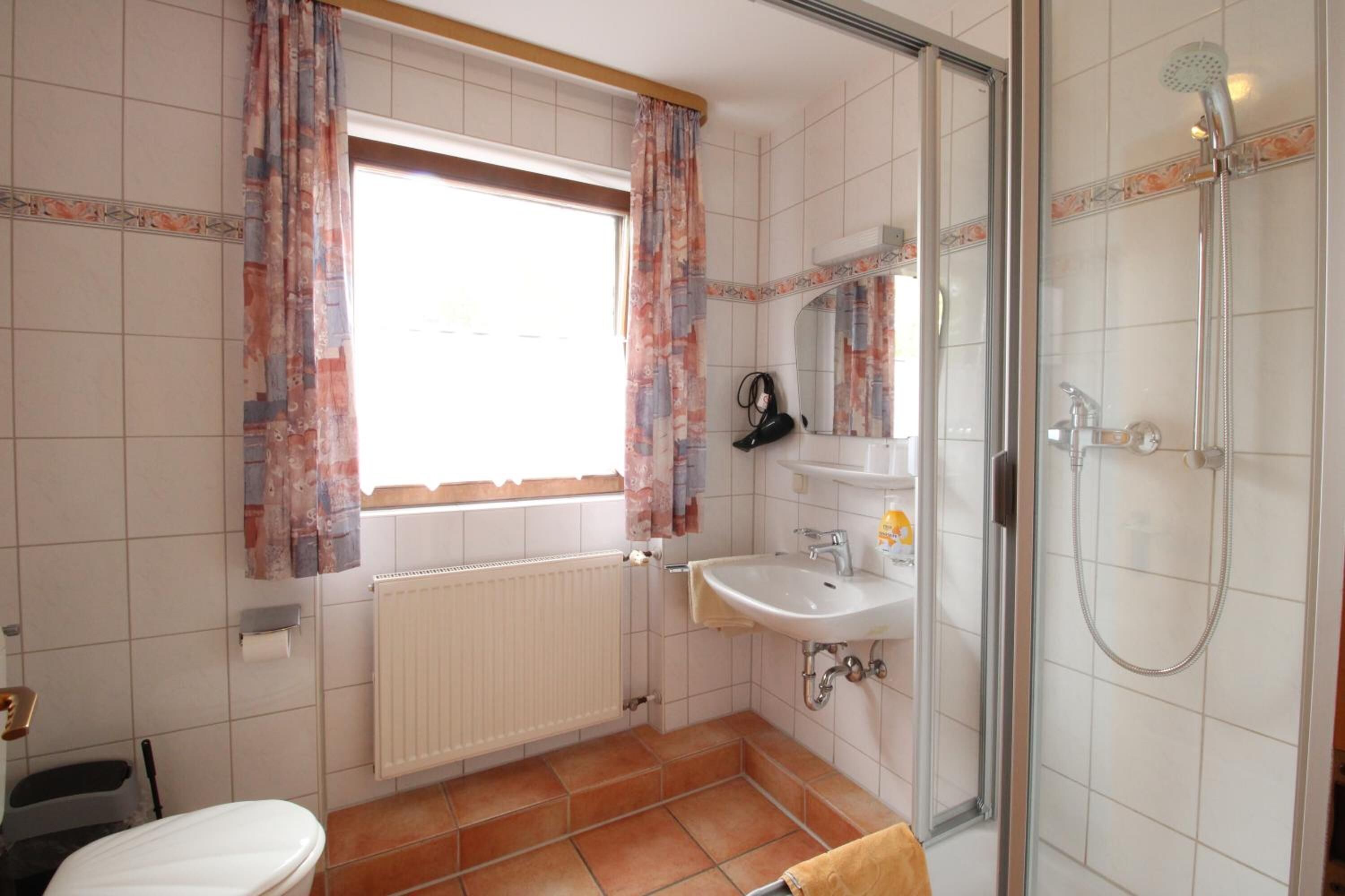 Ein Badezimmer mit Toilette, Waschbecken, Dusche und einem Fenster mit Vorhängen.