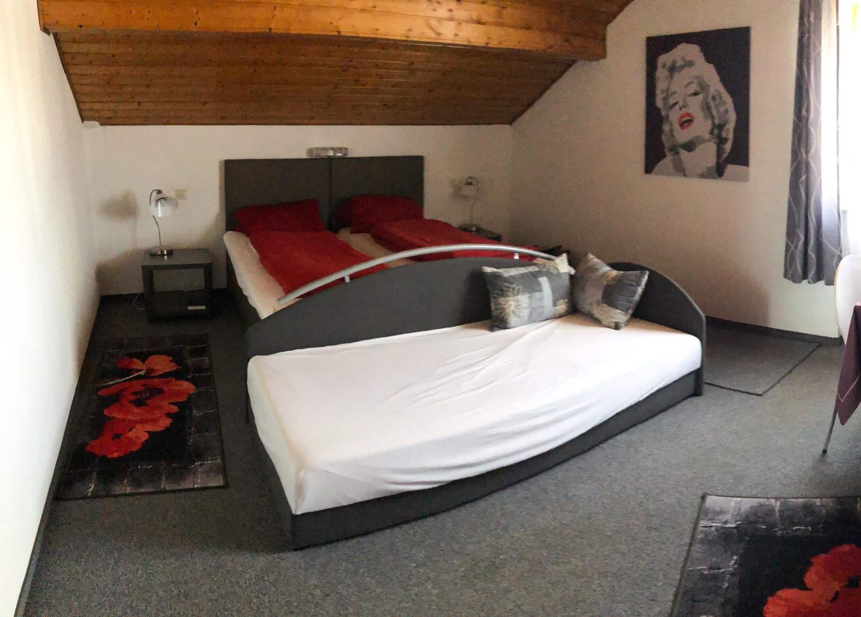 A bedroom with a large bed, two bedside tables, a red headboard, and a poster on the wall.