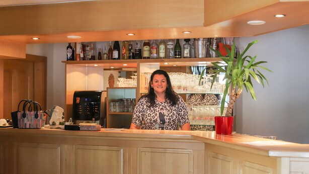 A bar area with a counter, shelves with bottles, a coffee machine, and a potted plant. - Zur Auszeit (Traunreut)