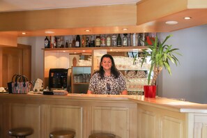 A bar area with a counter, shelves with bottles, a coffee machine, and a potted plant. - Zur Auszeit (Traunreut)