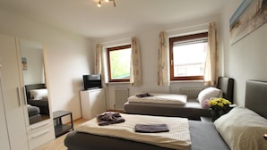 A bedroom with two beds, a TV, a mirror, and a window with curtains. - Zur Auszeit (Traunreut)