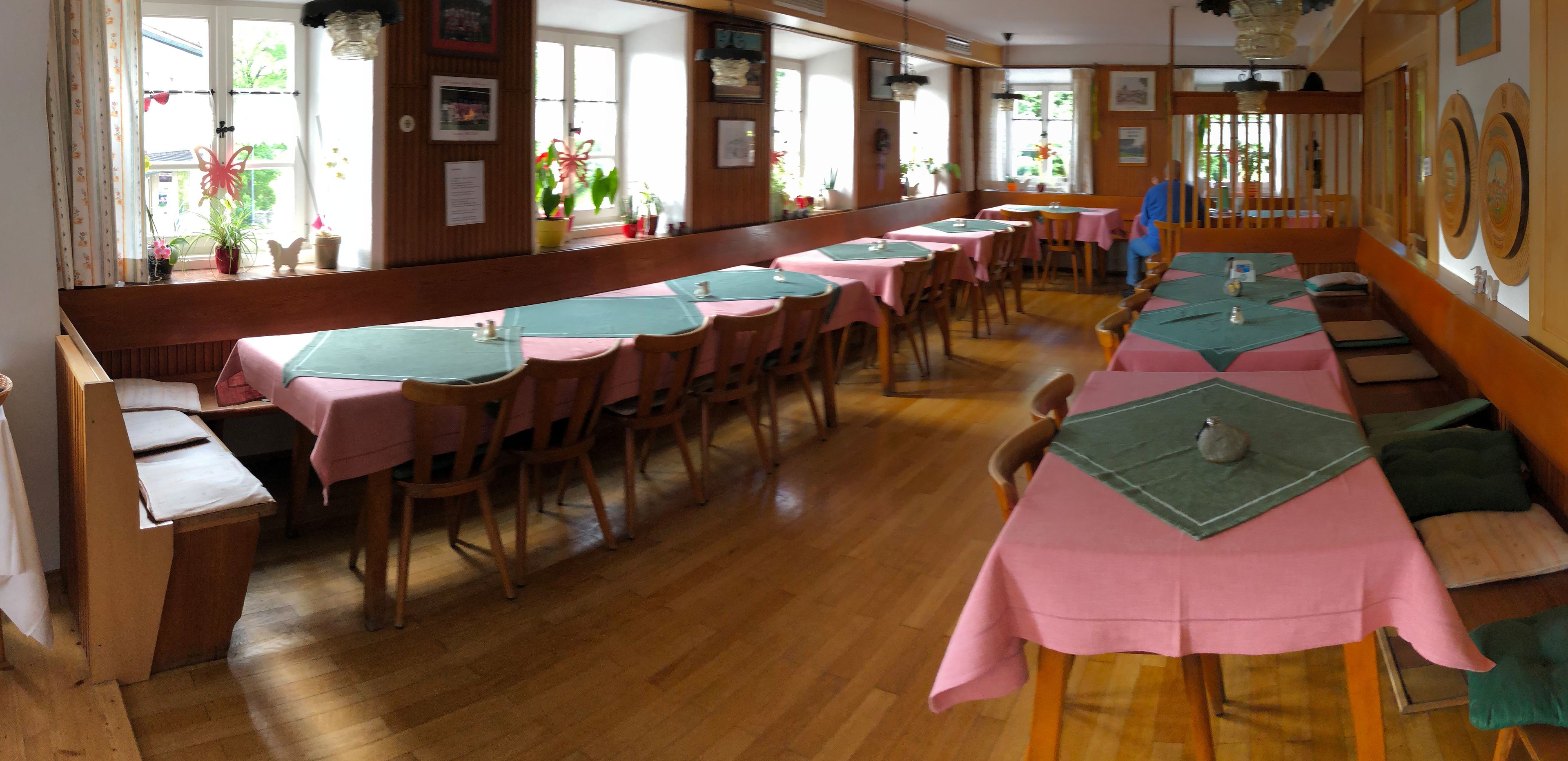 A dining area with long tables covered in pink tablecloths, wooden chairs, and benches.