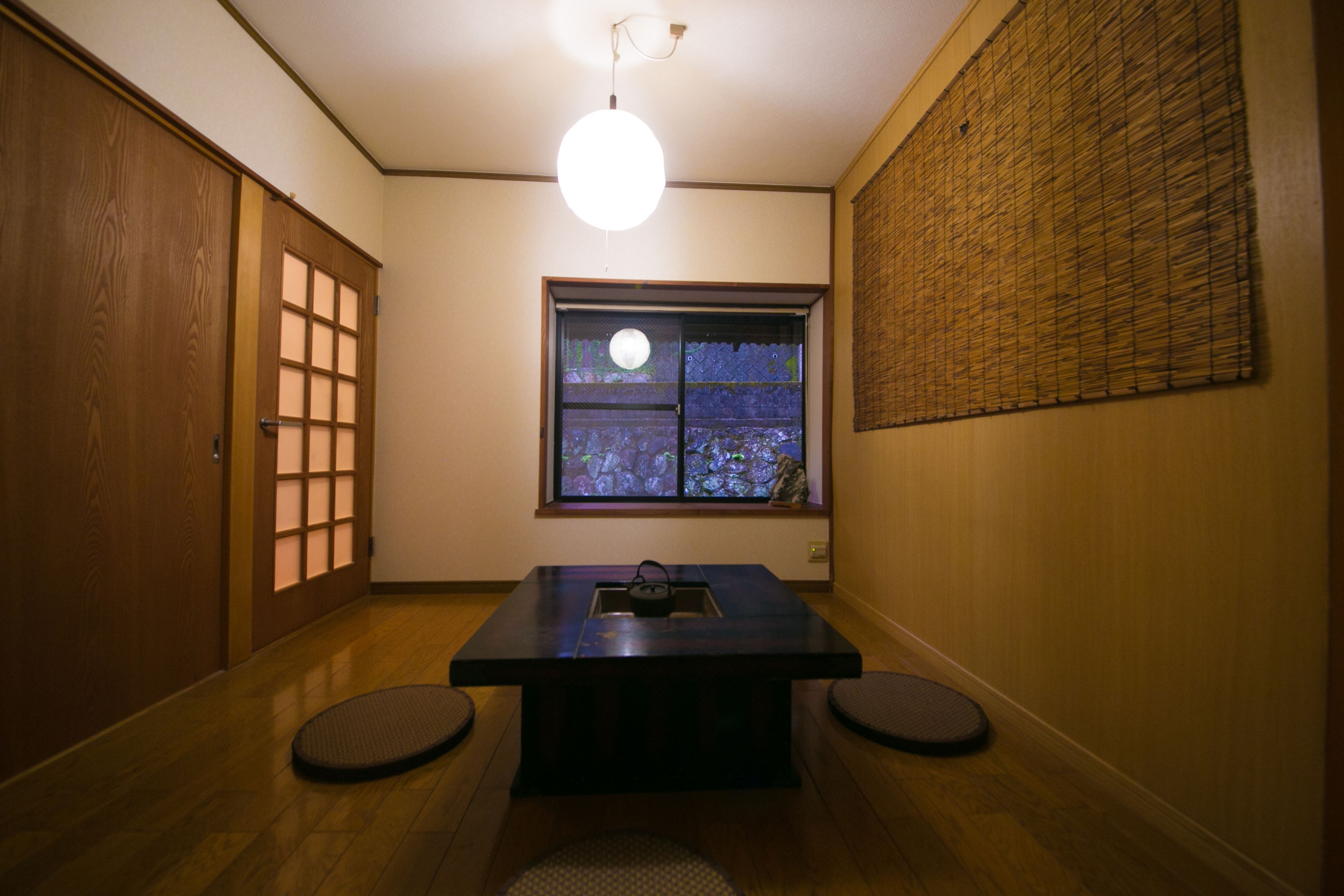 A traditional Japanese room with tatami flooring, a shoji screen window, and a low table with cushions.