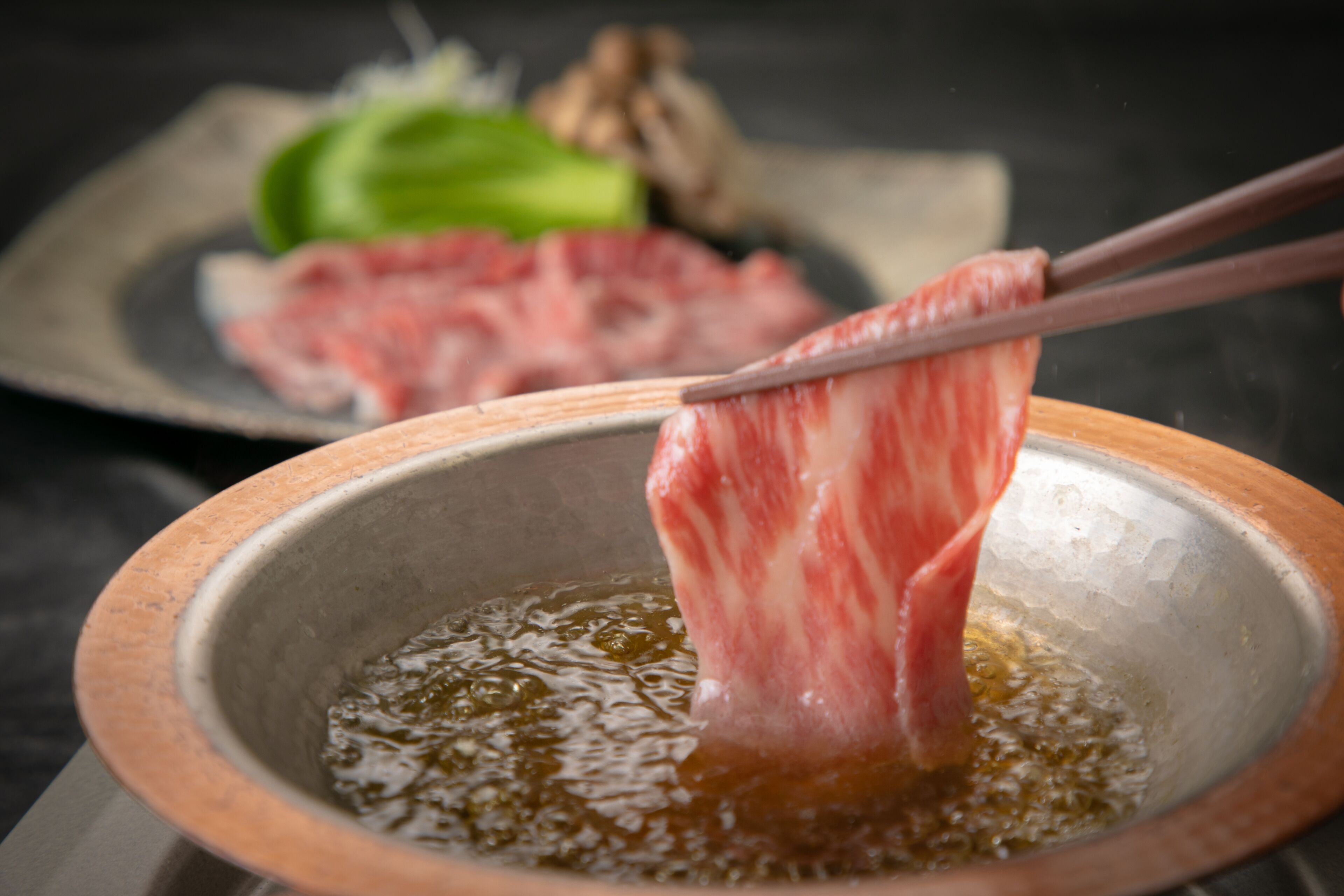 A bowl of hot oil with chopsticks holding a piece of meat.
