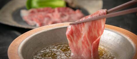 A bowl of hot oil with chopsticks holding a piece of meat.