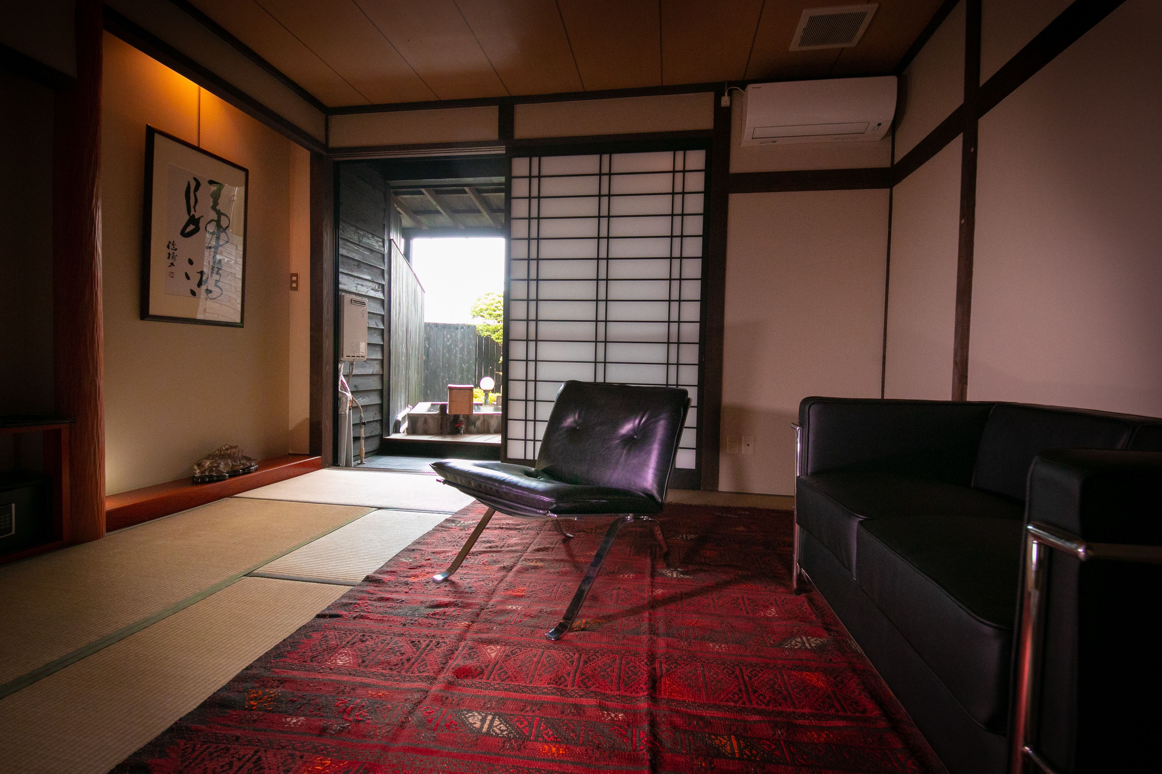 A traditional Japanese room with tatami flooring, a black leather chair, a black sofa, and a shoji screen door.