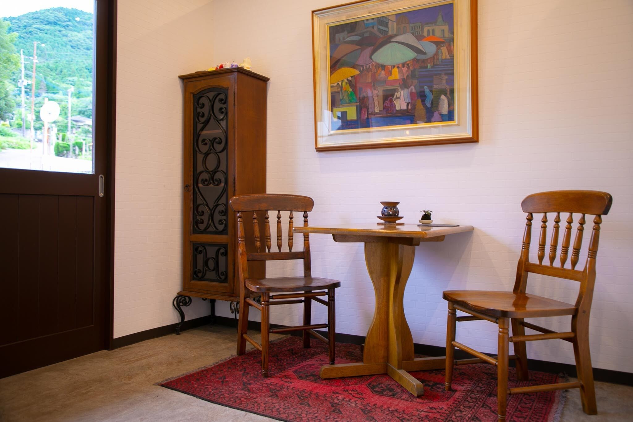 Une pièce comprenant un meuble en bois, deux chaises en bois, une petite table et un tableau encadré accroché au mur.