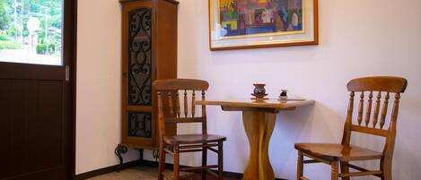 A room with a wooden cabinet, two wooden chairs, a small table, and a framed painting on the wall.