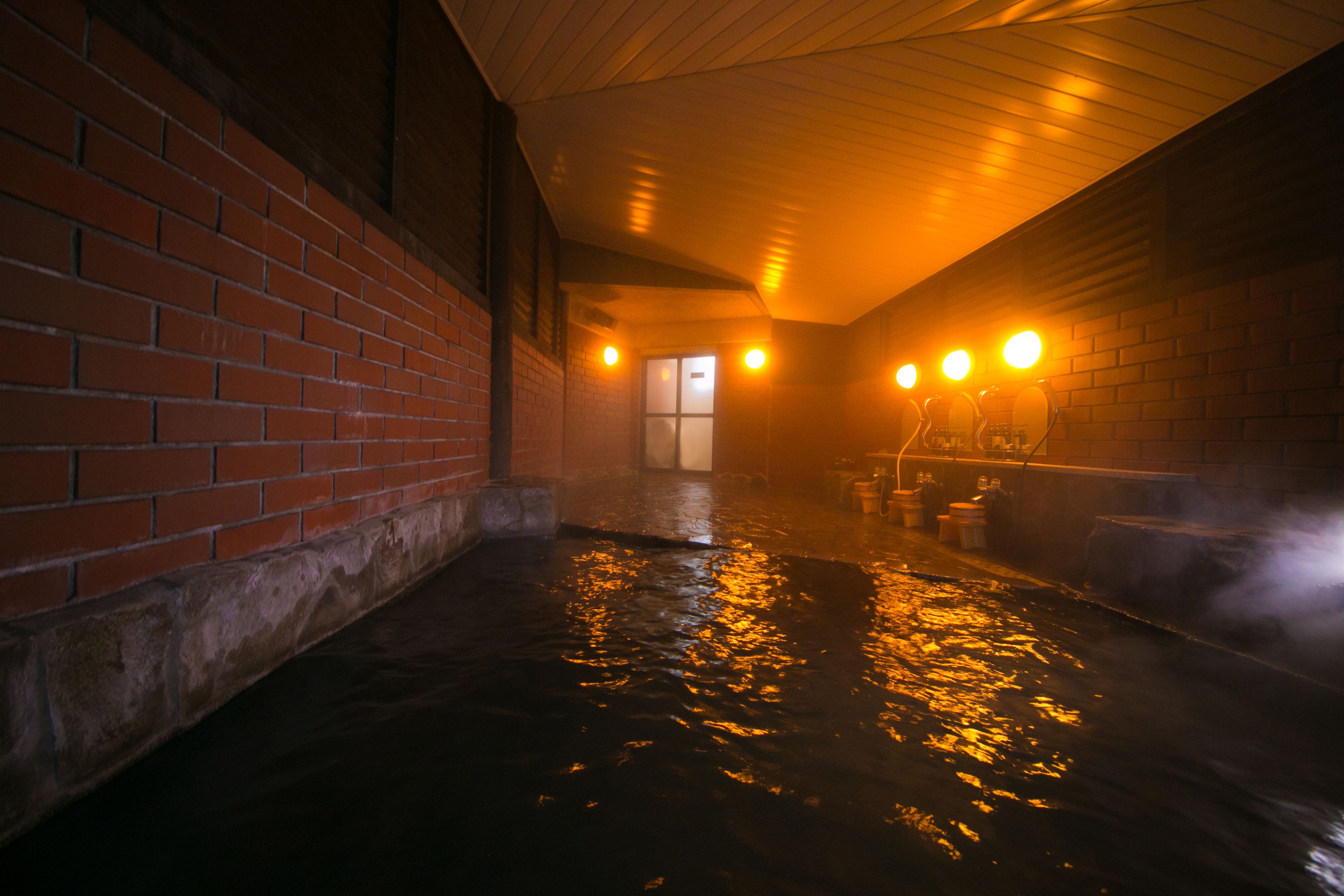 A steam room with brick walls, a wooden ceiling, and a wet floor reflecting light.