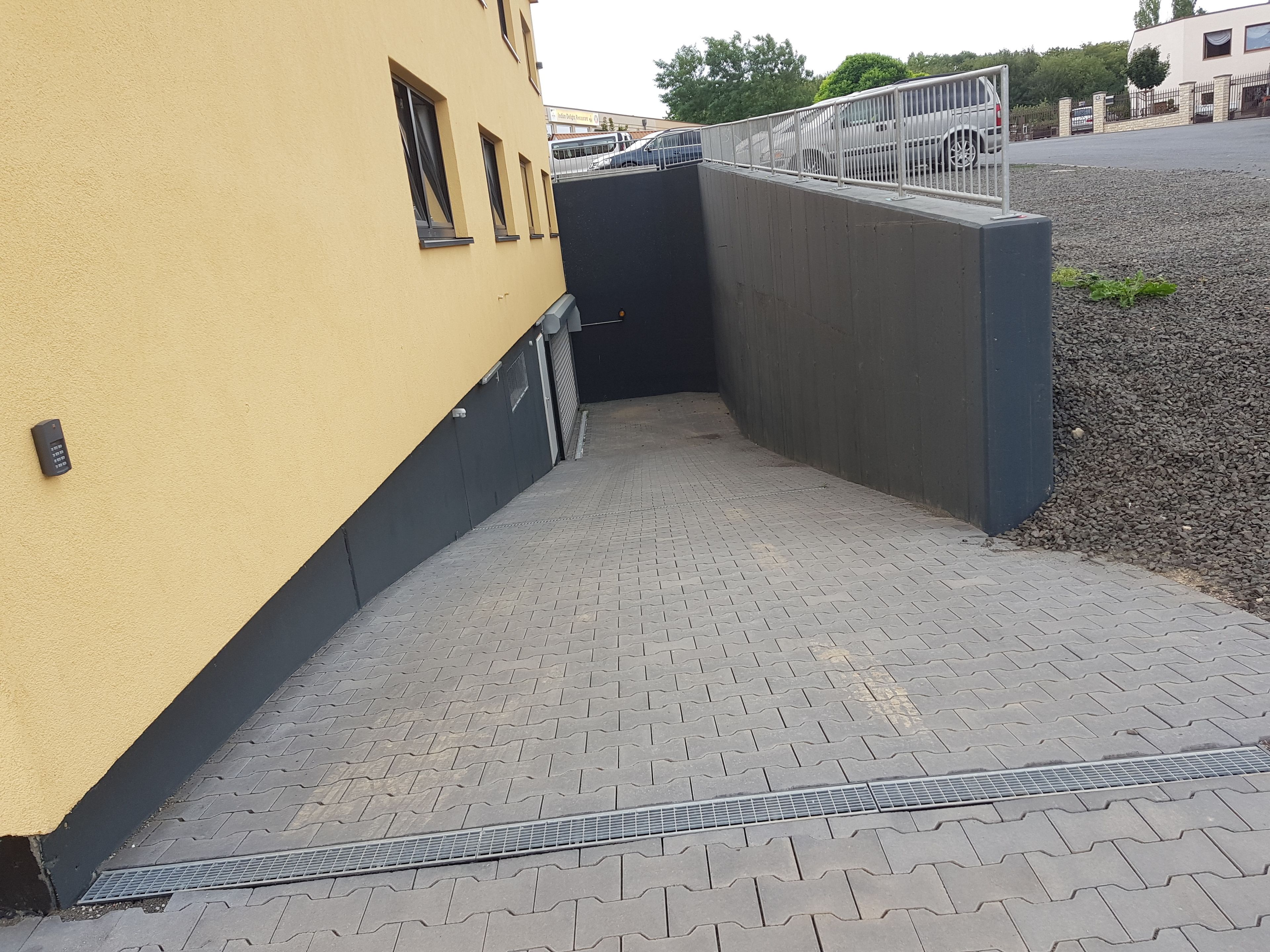 A paved pathway leading to a building entrance with a metal gate, a yellow wall, and a gravel area.
