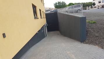 A paved pathway leading to a building entrance with a metal gate, a yellow wall, and a gravel area.