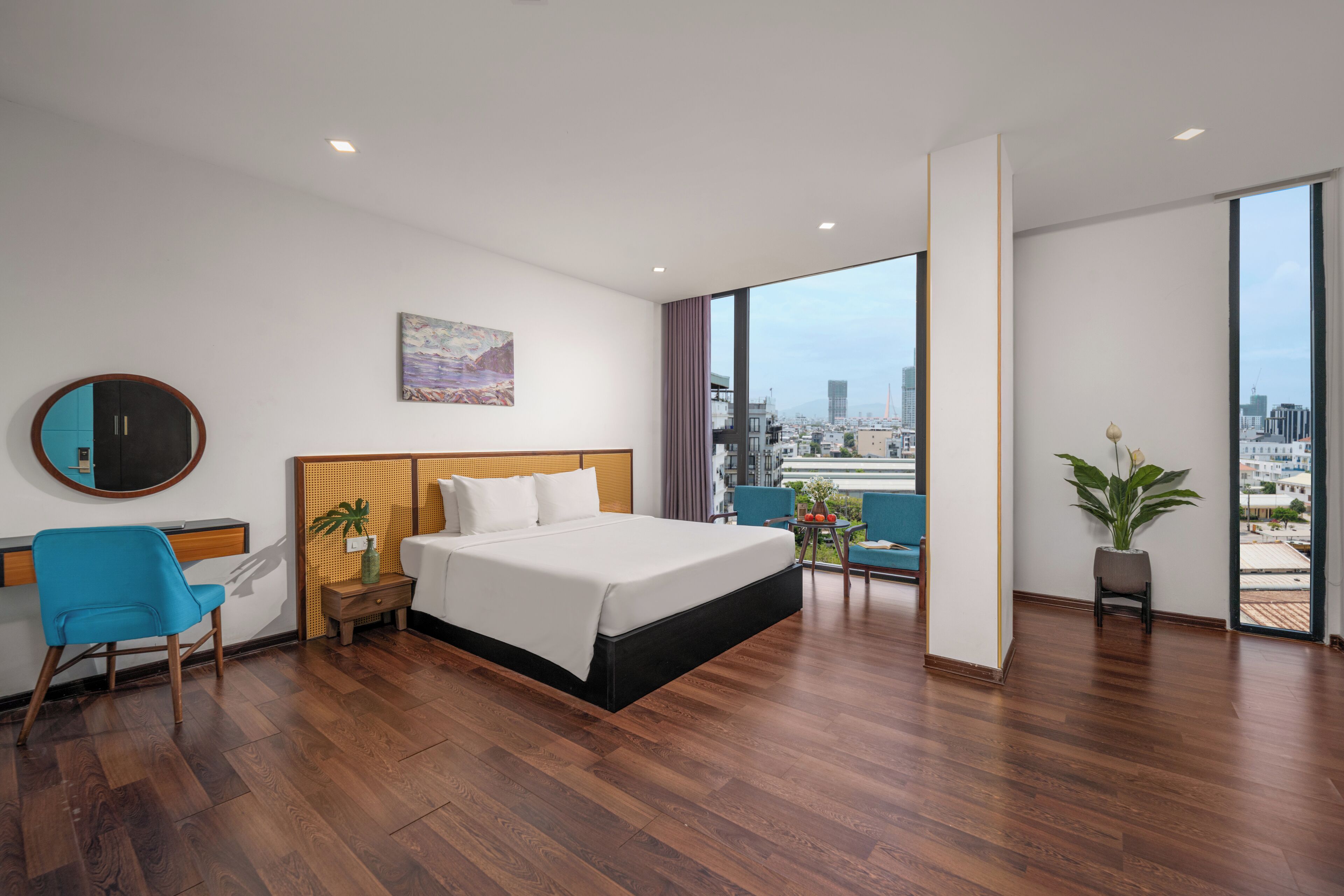 A modern hotel room with a large bed, a desk, a chair, and a balcony with a city view.