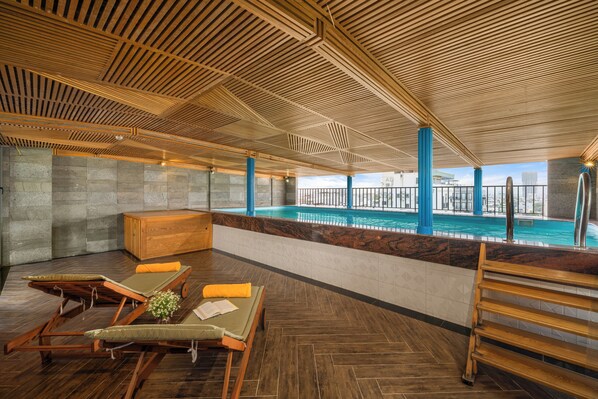 A poolside area with wooden loungers, a wooden bench, and a view of the pool. - Platinum Danang Hotel (Da Nang)