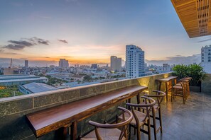 A rooftop bar with wooden seating and a cityscape view at sunset. - Platinum Danang Hotel (Da Nang)